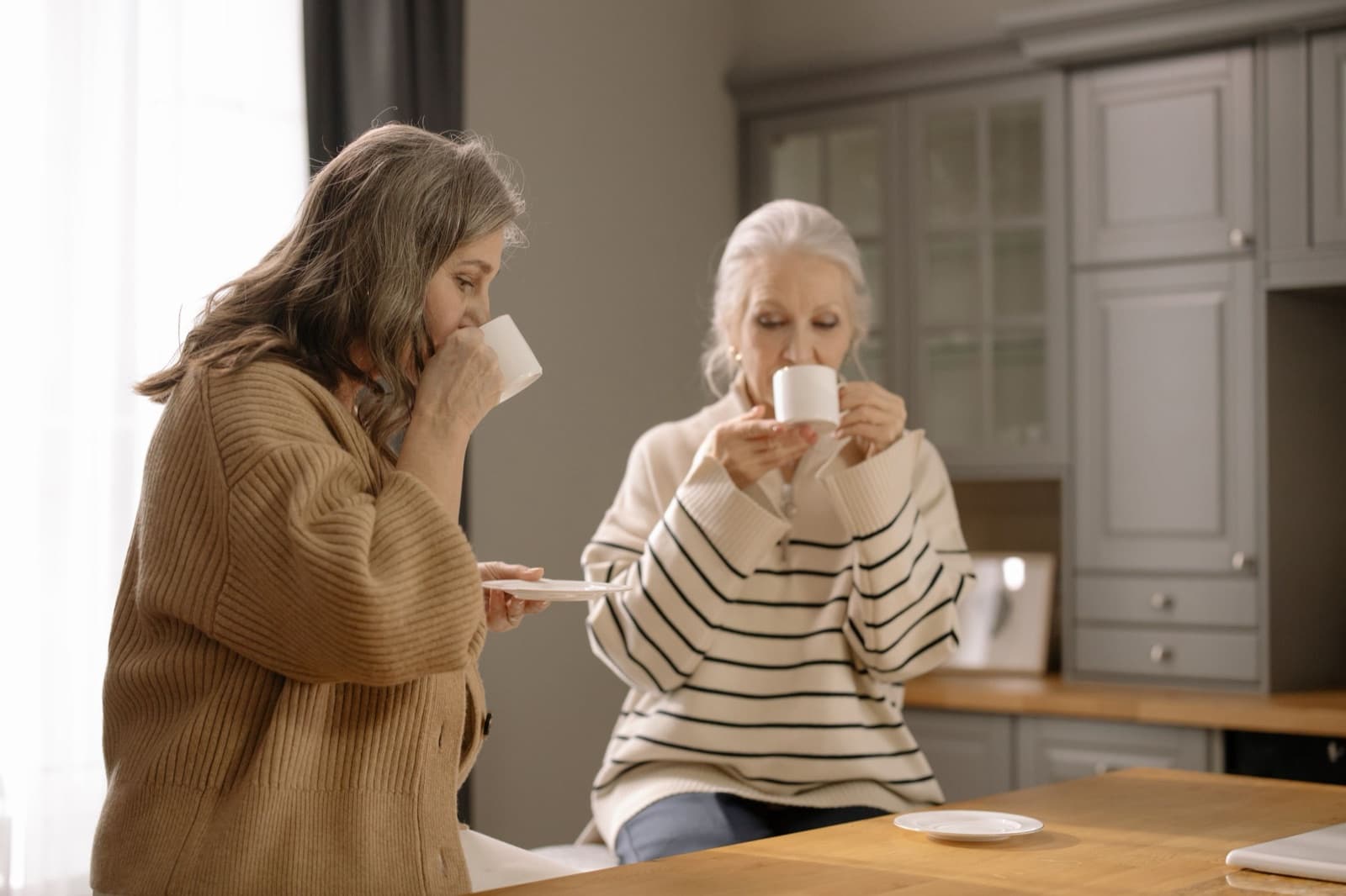 Een vrouw en haar oudere moeder drinken samen koffie aan de keukentafel
