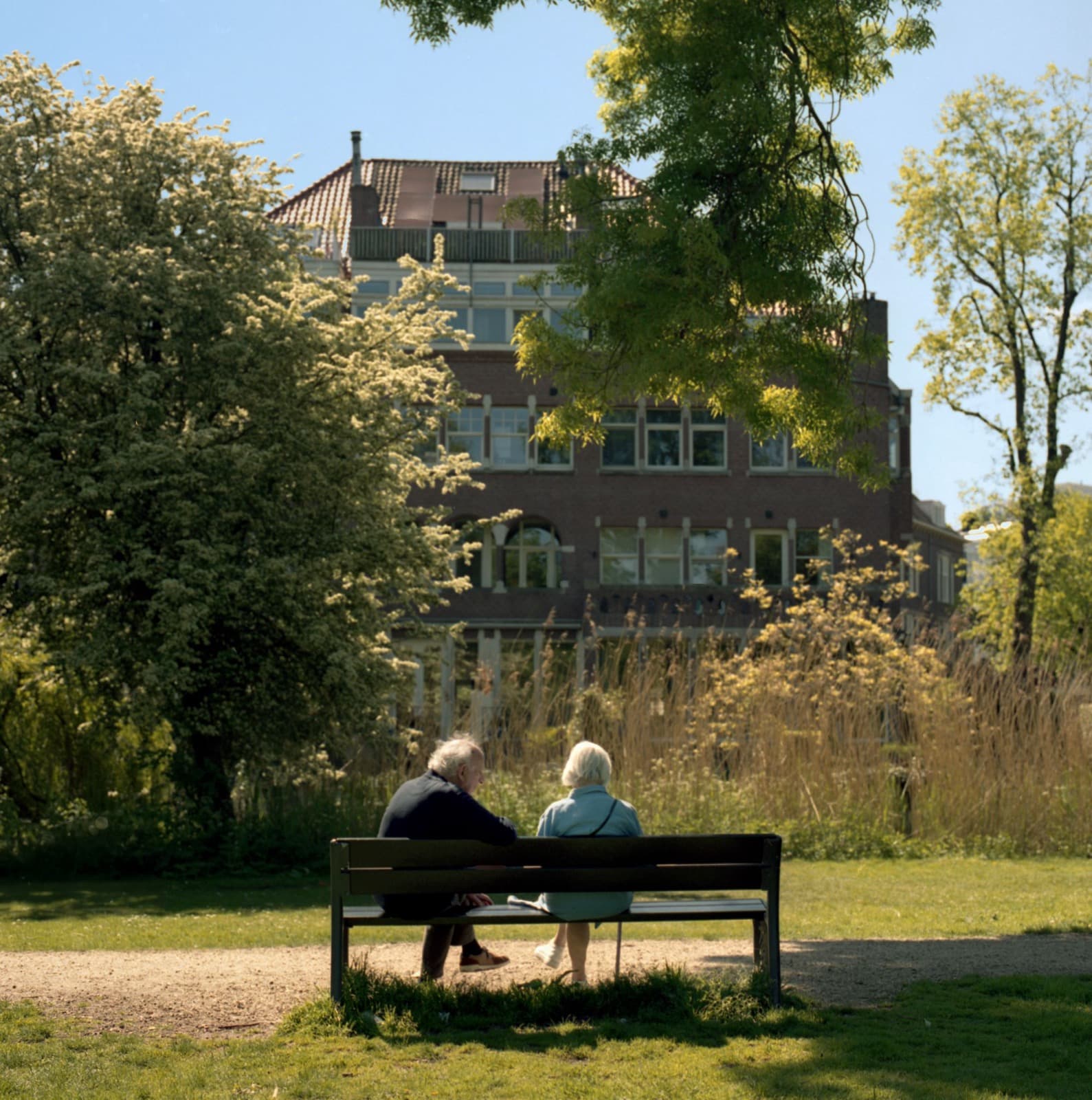 An older couple sit together on a bench in a sunny Dutch park