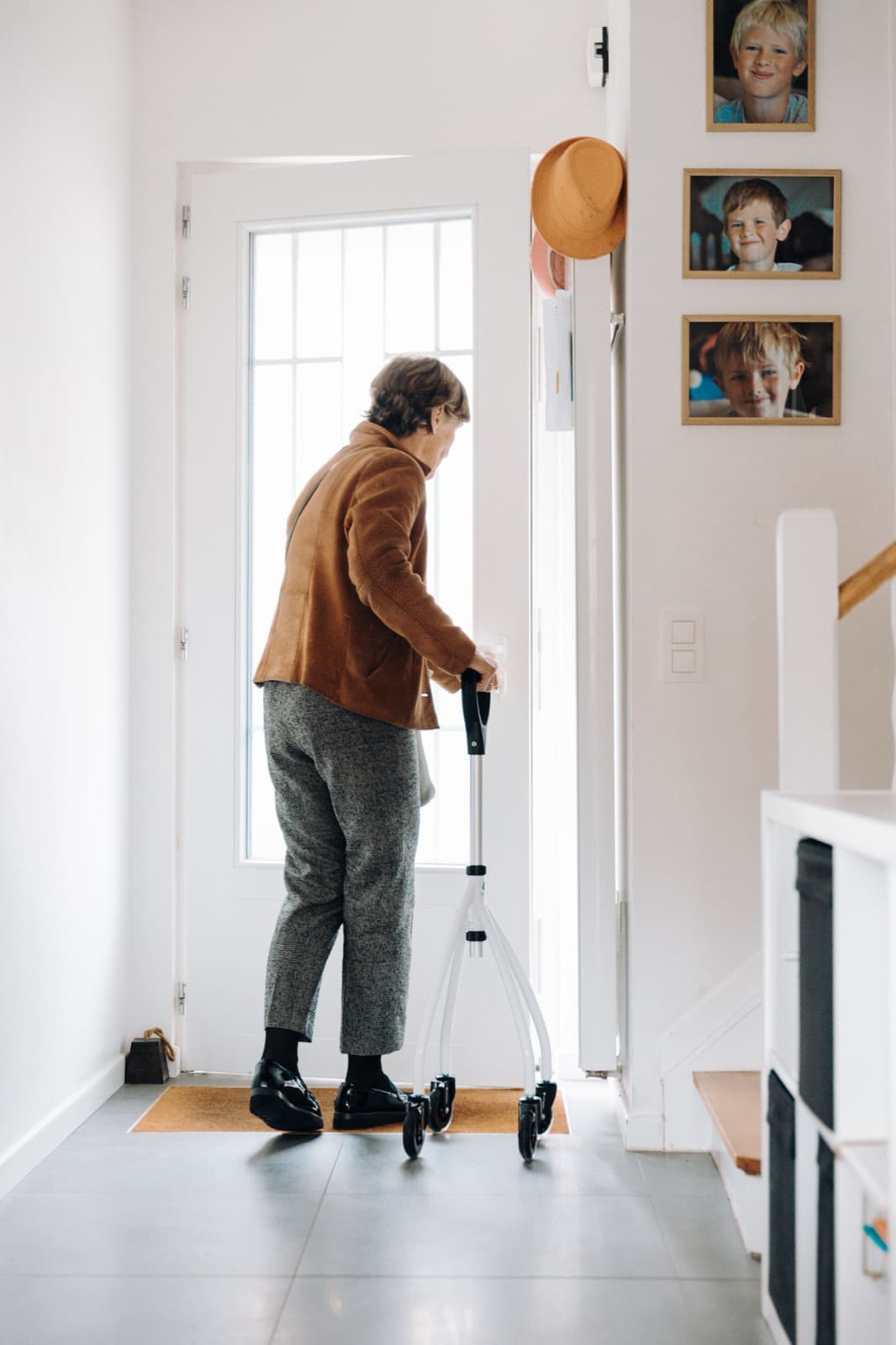 An older woman walks with a rollator towards the front door of her house