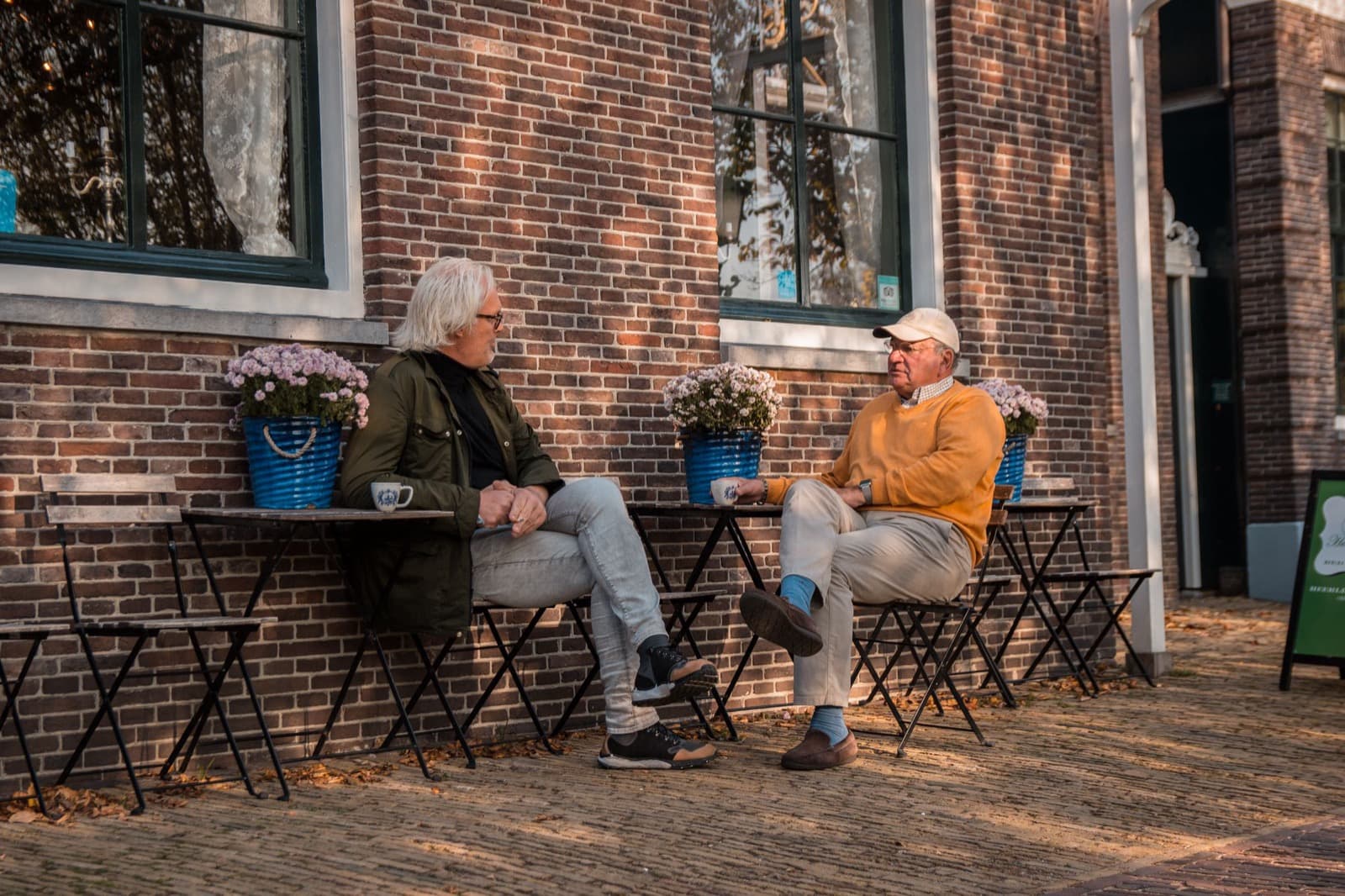Two older people drink coffee and talk on a terrace in their neighbourhood